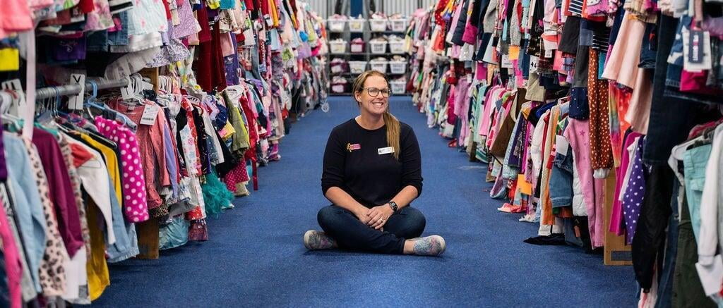 Owner of the JBF Gainesville JBF sale, Karen Miner, sits on the floor between racks of clothing.